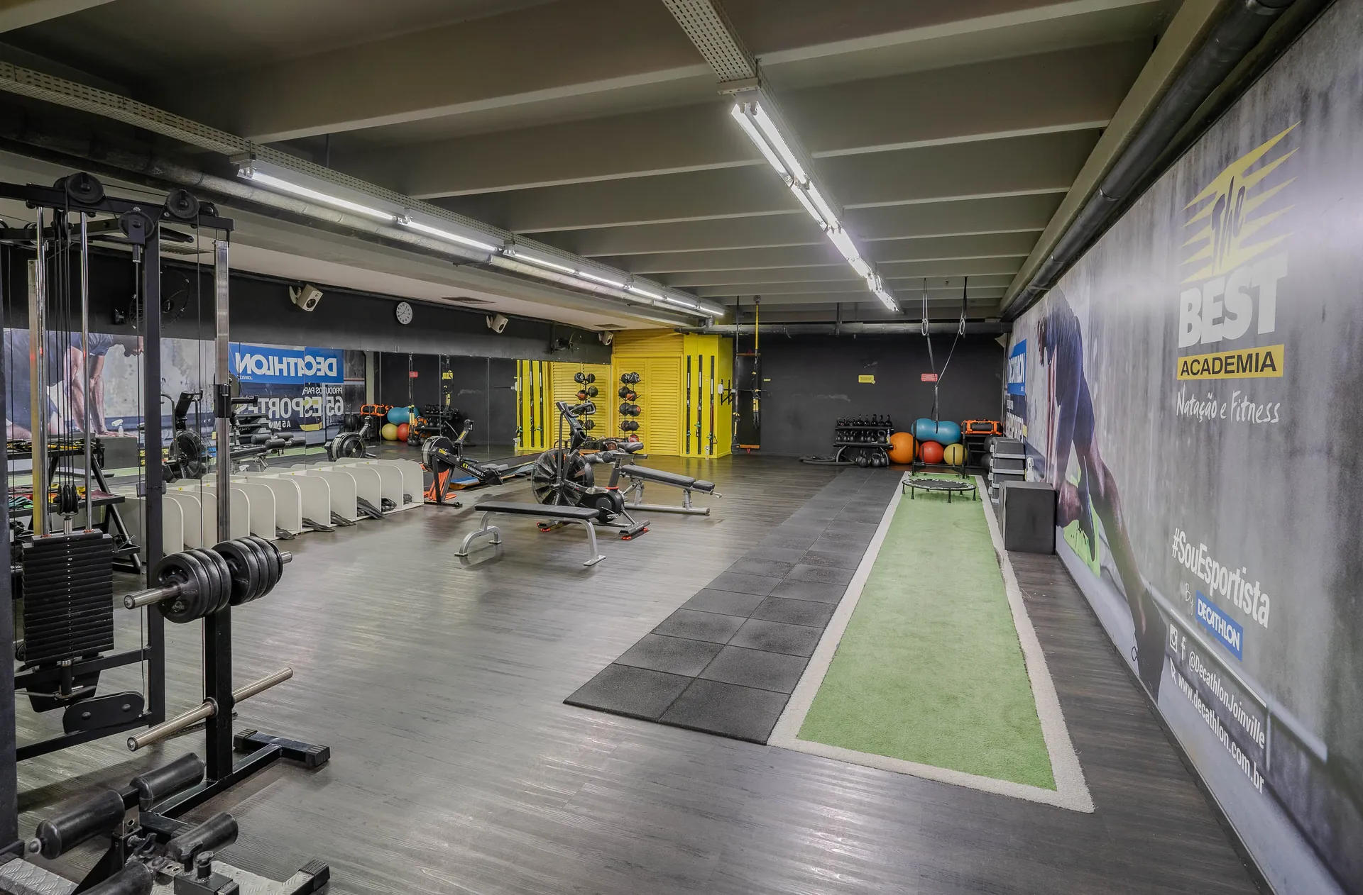 Área funcional da The Best, com pista de grama, racks e anilhas