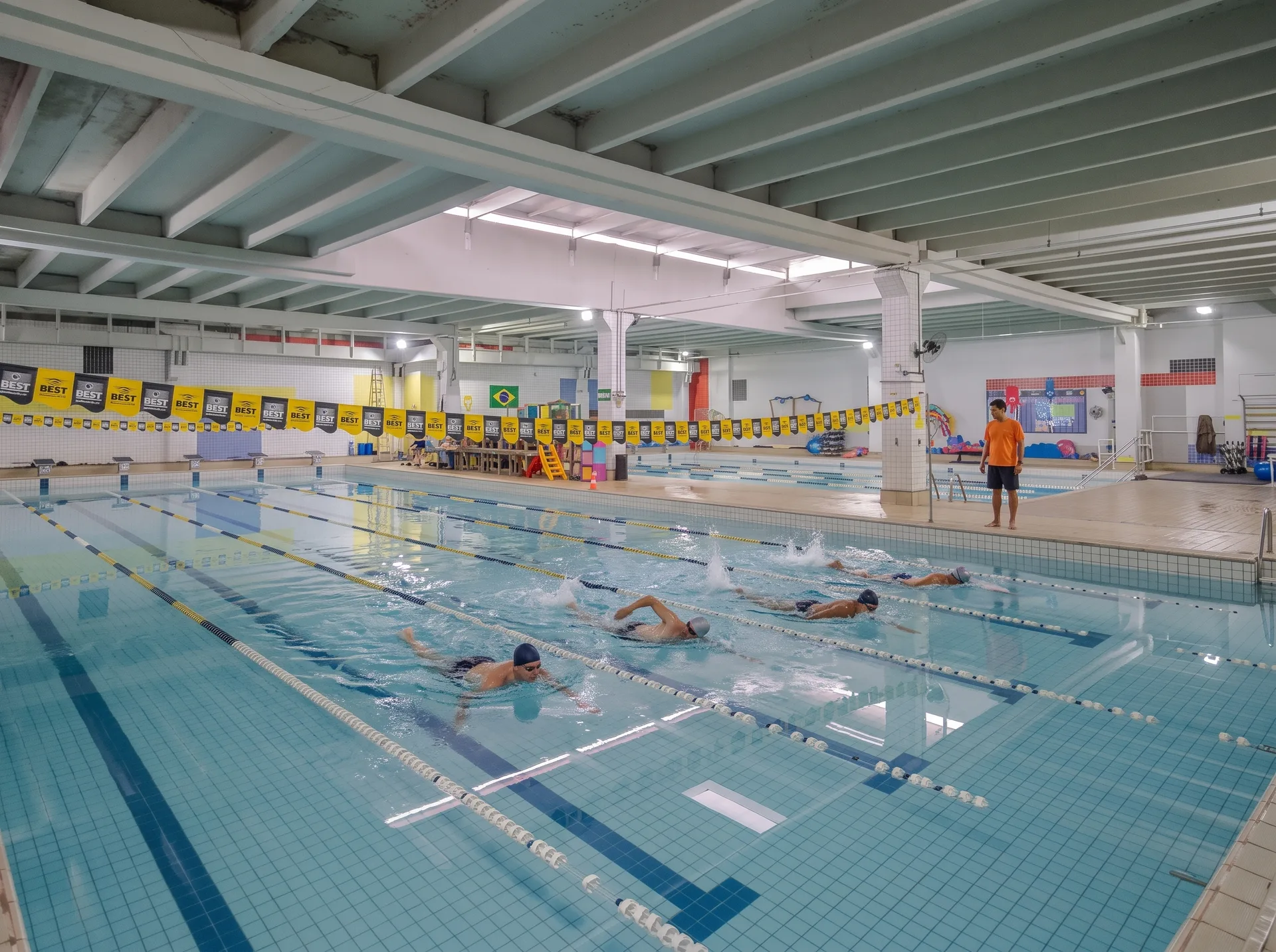 Nadadores de touca e óculos na piscina semiolímpica da The Best, com professor à disposição na borda